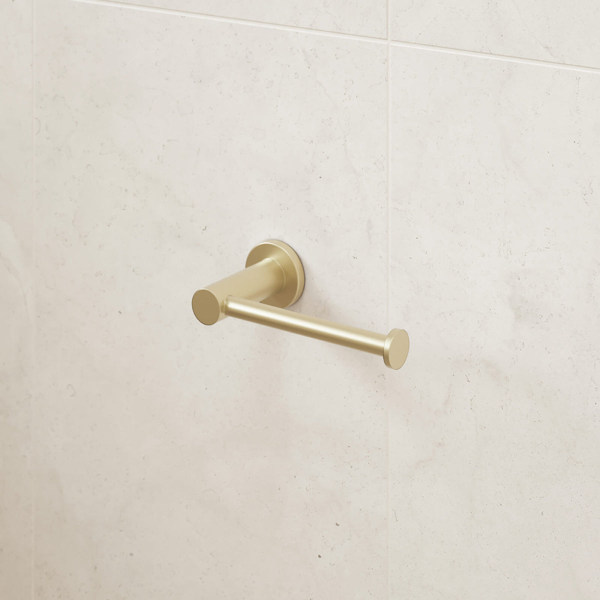 Caroma Liano II brushed brass toilet roll holder mounted on a light stone tile bathroom wall