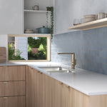 Caroma Luna II brushed brass sink mixer over a kitchen sink in a light timber benchtop and blue tiled kitchen.