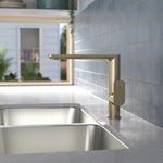 Caroma Luna II brushed brass sink mixer on a kitchen benchtop beside a stainless steel sink, side view