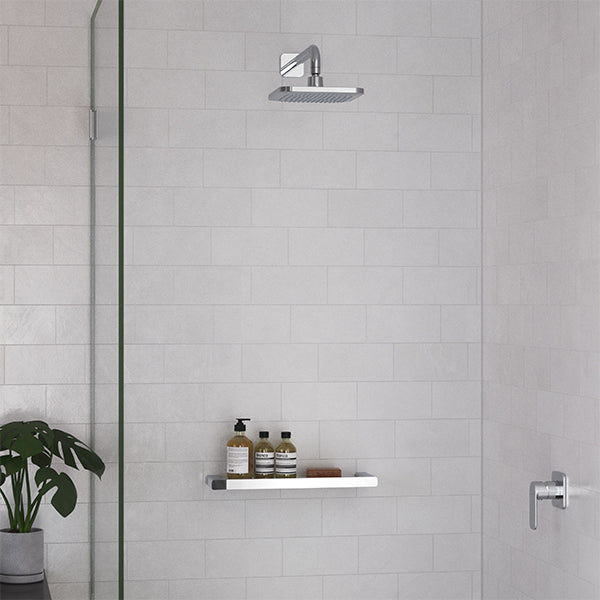 Caroma Luna chrome square overhead shower head in a tiled shower, wall-mounted with matching arm and shelf below