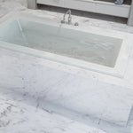 Caroma Newbury white rectangular island bath inset in marble-look tiled hob with centre tap and waste holes