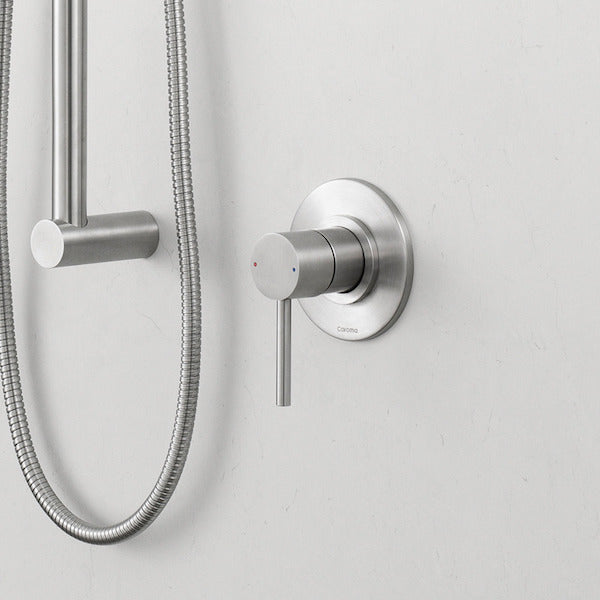 Caroma Titan stainless steel bath/shower mixer with round wall plate and lever handle, shown installed beside a shower hose on a white wall