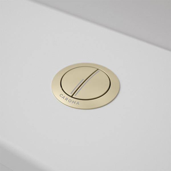 Caroma round metal cistern flush button in brushed brass on a white toilet cistern, top view