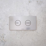 Caroma white dual flush toilet button plate on stone-look wall, rectangular concealed cistern flush panel, front view