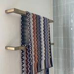 Caroma Urbane II double towel rail in brushed brass, mounted on a bathroom wall with two striped towels