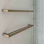 Caroma Urbane II double towel rail in brushed brass on a bathroom wall, showing two slim rails in a modern rectangular design