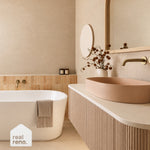 Caroma white oval freestanding bath in a beige bathroom setting, with brass tapware and towel draped over the rim
