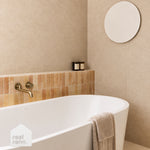 Caroma Urbane II white freestanding oval bath in a beige tiled bathroom with brushed brass tapware