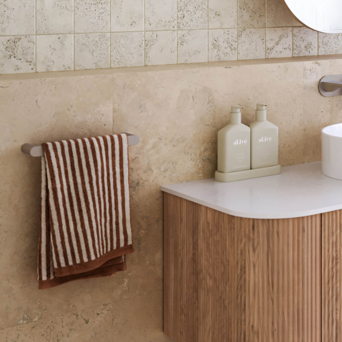 Caroma Urbane II gunmetal hand towel rail mounted on a bathroom wall, holding a striped towel beside a vanity