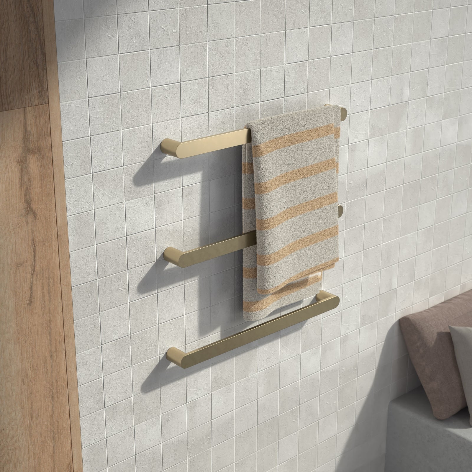 Caroma Urbane II brushed brass heated towel rail with three horizontal bars holding a striped towel on tiled wall