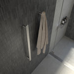 Caroma Urbane II vertical heated towel rail in polished stainless steel, shown mounted on a dark tiled bathroom wall with towel.
