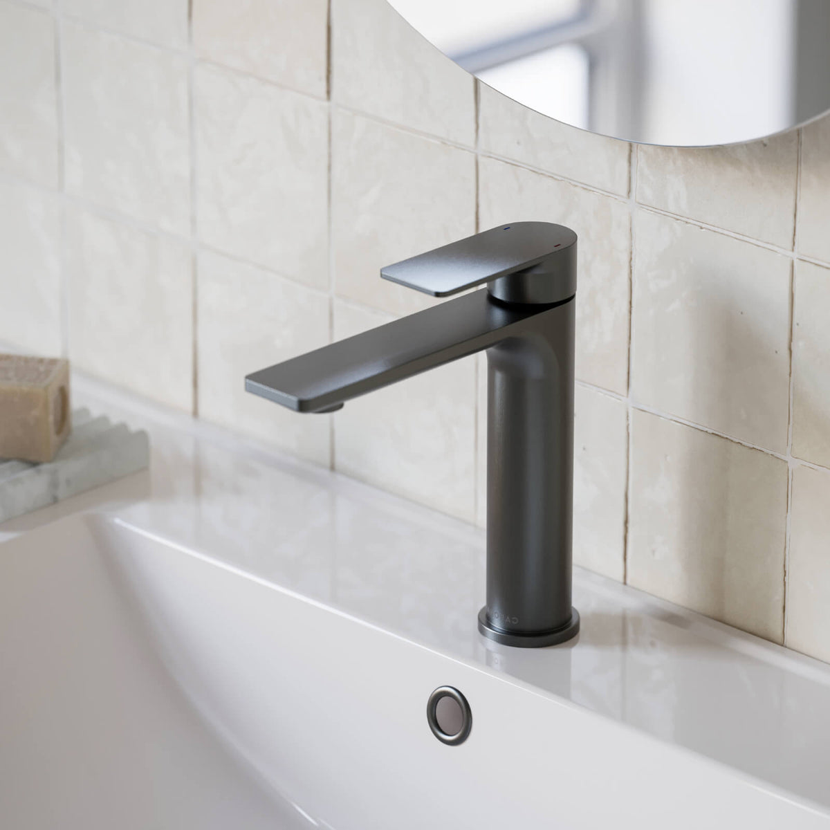 Caroma Urbane II mid tower basin mixer in gunmetal, hob mounted on a white basin beside tiled bathroom wall