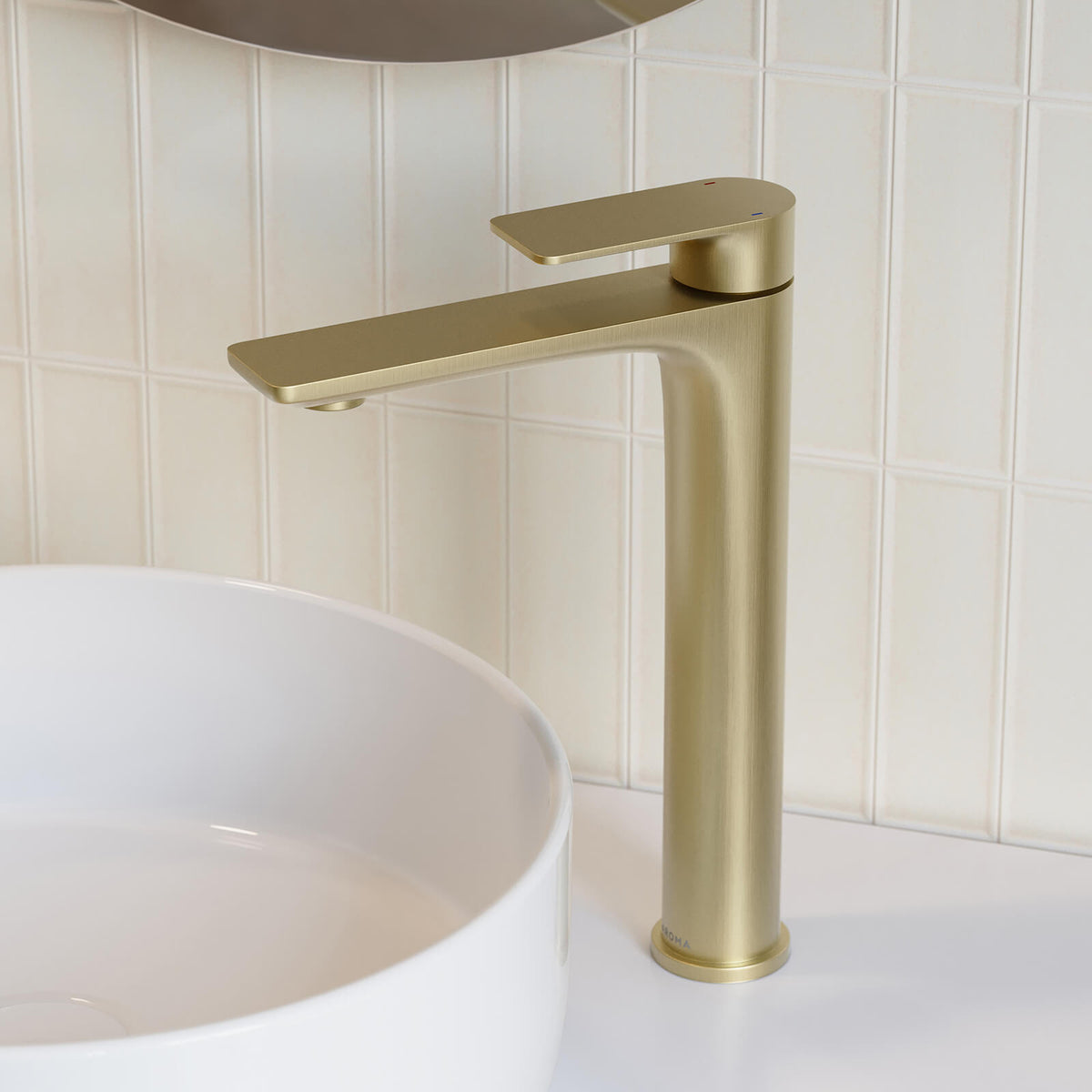 Caroma Urbane II tower basin mixer in brushed brass, shown installed beside a white basin on a tiled bathroom wall