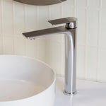 Caroma Urbane II tall chrome basin mixer beside a white vessel basin on a tiled bathroom vanity