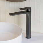Caroma Urbane II tower basin mixer in gunmetal, shown with a white above-counter basin on a tiled bathroom vanity.
