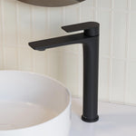 Caroma Urbane II tower basin mixer in matte black, shown beside a white vessel basin on a bathroom vanity