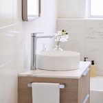 Caroma Urbane II chrome tower basin mixer on a bathroom vanity beside a white fluted vessel basin, side view