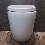 Fienza Aluca back-to-wall toilet suite in gloss white with slim closed seat, front view against dark tiled wall.