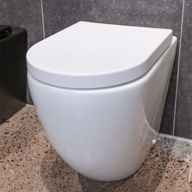 Fienza Aluca wall-faced toilet suite in gloss white with slim seat, shown installed against tiled wall and terrazzo floor