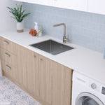 Fienza Hana stainless steel laundry sink installed in a white benchtop, with chrome mixer tap and light timber cabinetry