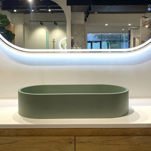 Fienza Jada sage concrete above-counter pill basin, oval 600mm, displayed on a vanity in a showroom