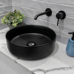 Fienza Kaya wall basin mixer set in matte black with round plates and curved spout above a black vessel basin