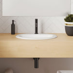 Fienza Kaya matte black basin mixer on a timber vanity beside a white basin, with matching black bottle trap and spout