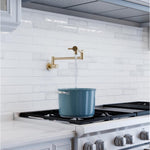 Fienza Kaya wall-mounted pot filler in gun metal above a cooktop, filling a stockpot against white subway tiles