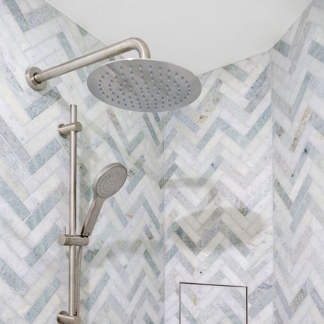 Fienza Kaya brushed nickel shower arm with round shower head in a tiled bathroom wall setting