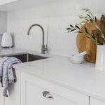 Fienza Kaya brushed nickel gooseneck sink mixer in a white kitchen, side view over a stainless steel sink