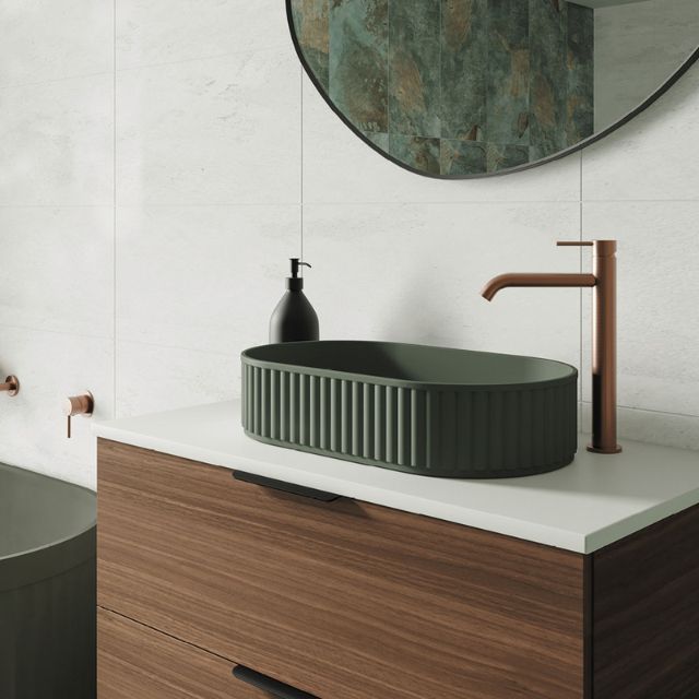 Fienza Kaya tall basin mixer in brushed copper, shown mounted beside a green vessel basin on a vanity