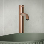 Fienza Kaya tall basin mixer in brushed copper, mounted above a matte green vessel basin