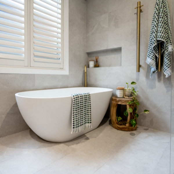 Fienza Nero matte white freestanding stone bath in a modern bathroom, oval shape with towel draped over side