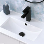 Fienza matte black pop-up basin waste with plug in a white bathroom basin, beneath matching tapware