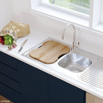 Fienza oak sink chopping board over a stainless steel kitchen sink, with knife and produce on a white benchtop
