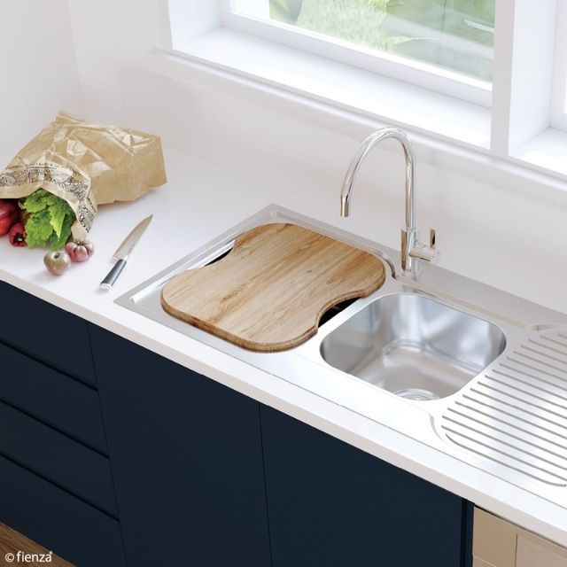 Fienza oak sink chopping board over a stainless steel kitchen sink, with knife and produce on a white benchtop
