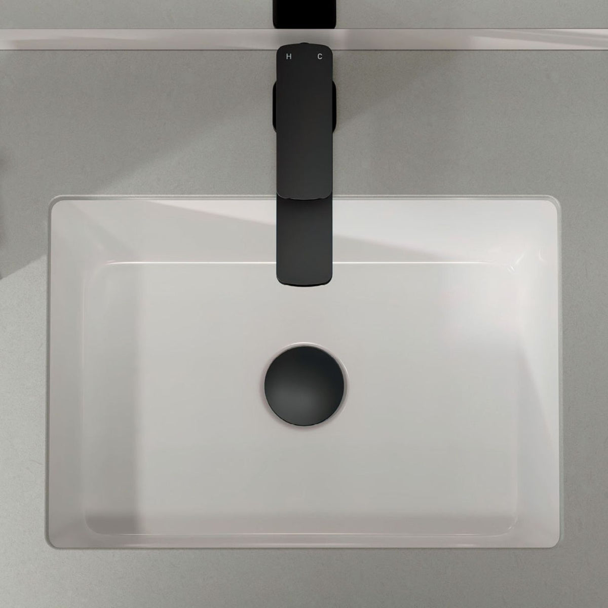Fienza Tono matte black basin mixer installed over a white square basin, top view, showing the flat square spout and mixer lever.