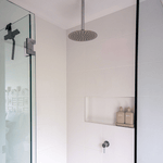 Chrome ceiling shower arm with round rainfall shower head in a white tiled shower nook, front view