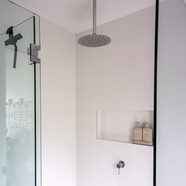 Chrome ceiling shower arm with round rainfall shower head in a white tiled shower nook, front view