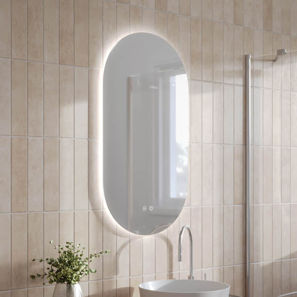 Ingrain pill-shaped frameless backlit LED mirror, portrait wall-hung, lit in a beige tiled bathroom vanity setting