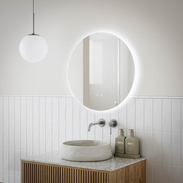 Ingrain round frameless backlit LED mirror above bathroom vanity, shown lit in a modern white tile setting