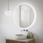 Ingrain round frameless backlit LED mirror above wall-hung basin in a modern bathroom, with white tiles and pendant light