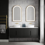 Brushed gold Phoenix Cromford heated towel ladder on black wall, holding grey towels in a modern bathroom vanity setting