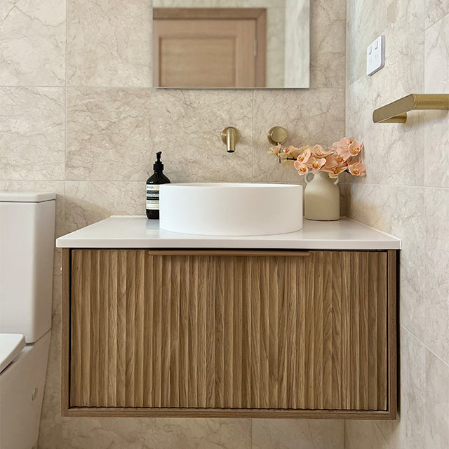 Marquis Cove wall hung vanity with fluted timber grain finish, white top and round basin, in a beige bathroom setting
