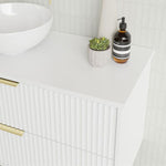 Marquis Lake wall hung vanity with white benchtop, ribbed front panels and brass handles, styled with basin, soap dispenser and plant