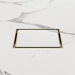 Nero square tile insert floor waste in brushed gold, shown flush set into white marble-look tiles.