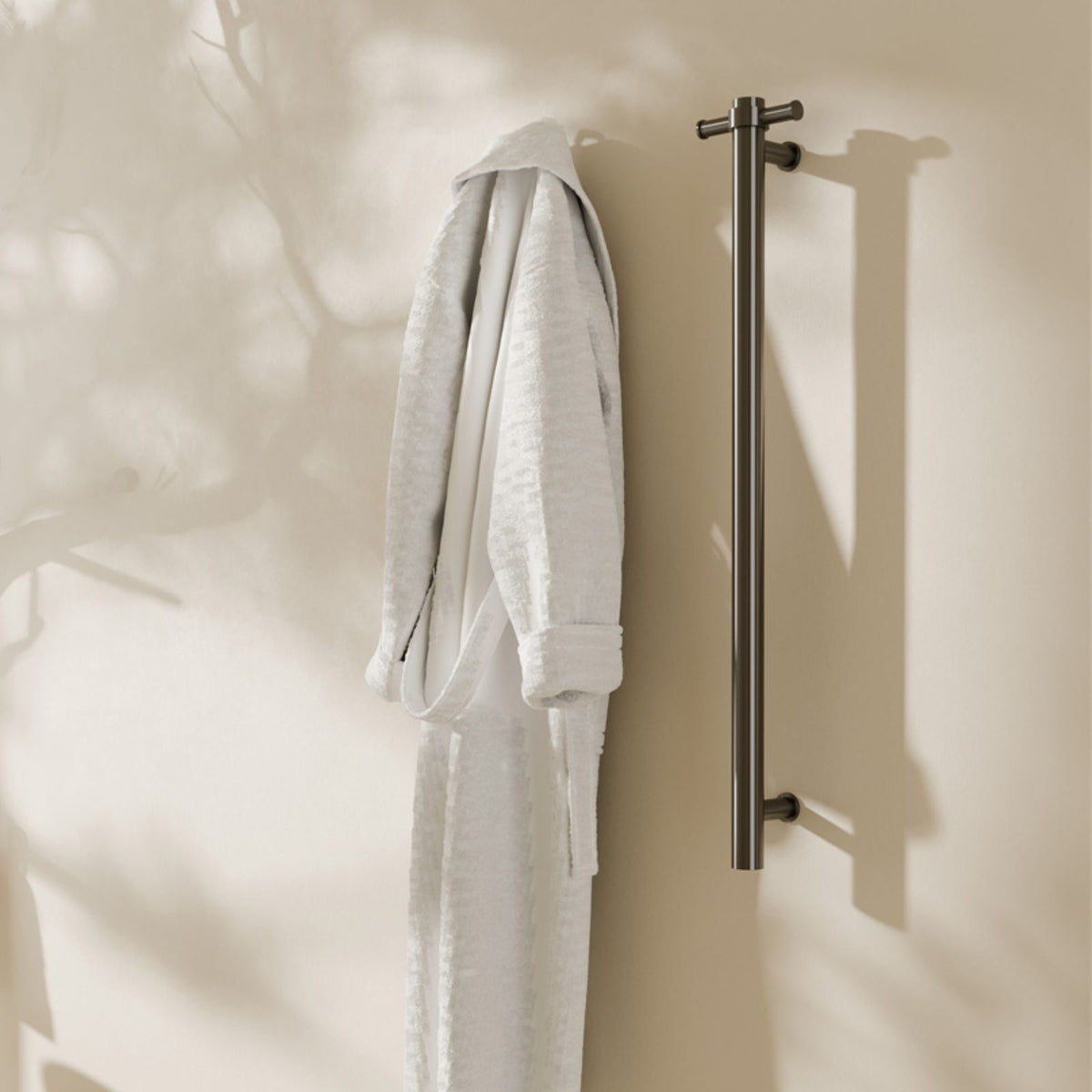 Nero Mecca single vertical heated towel rail in gun metal, wall mounted with white robe in a bathroom setting
