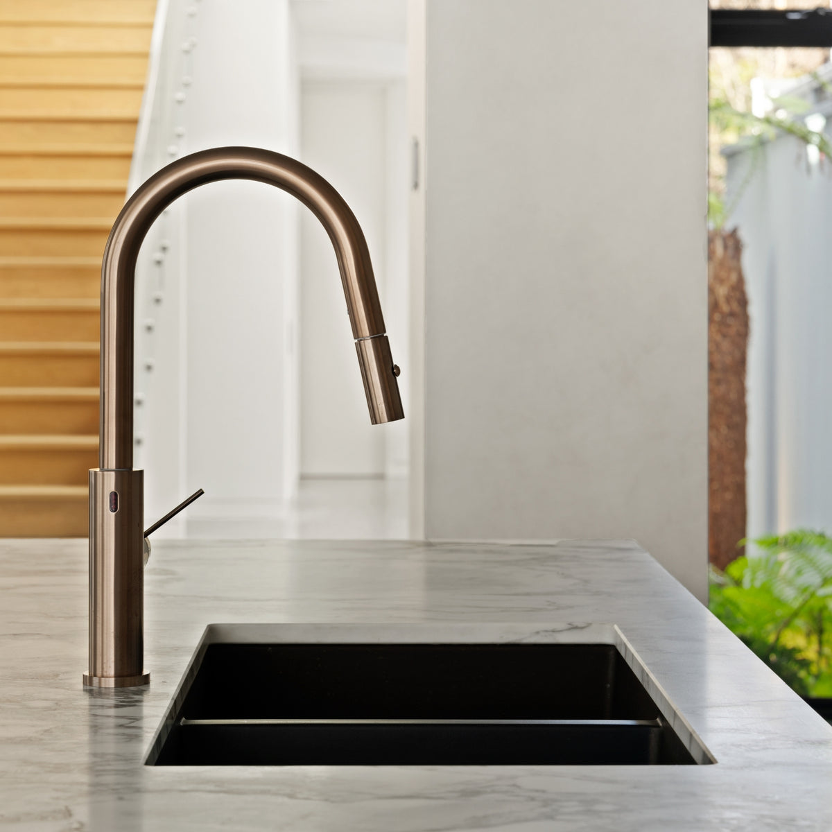 Nero Mecca Smart Sensor pull out kitchen mixer in brushed bronze, hob mounted over a black sink on a stone benchtop