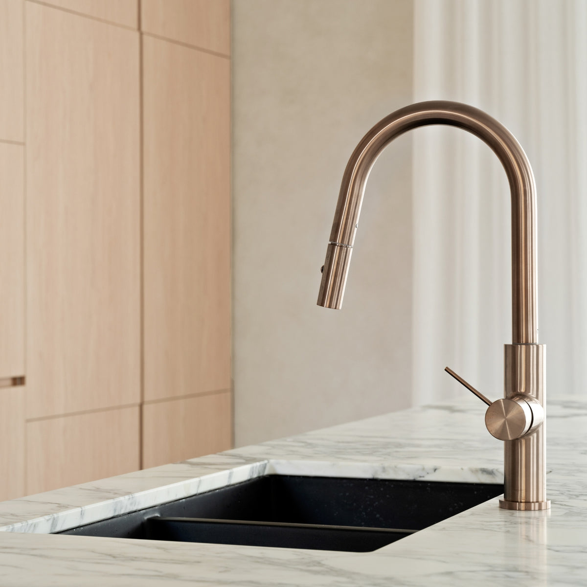 Nero Mecca pull out kitchen mixer in brushed bronze, shown mounted on a marble-look benchtop with black sink in kitchen setting