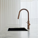 Nero Mecca brushed bronze pull out kitchen mixer with arched spout and single lever on a marble benchtop above a black sink